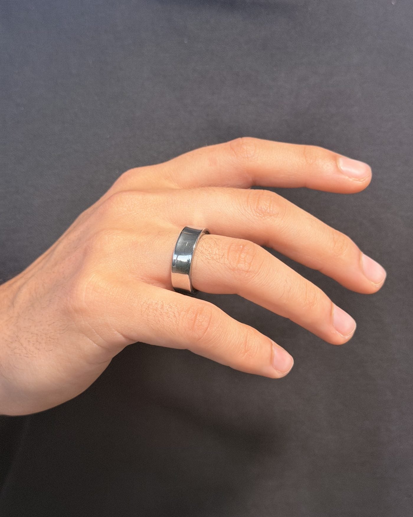 A hand wearing the silver Mudrika Ring on the middle finger, against a plain charcoal t-shirt
