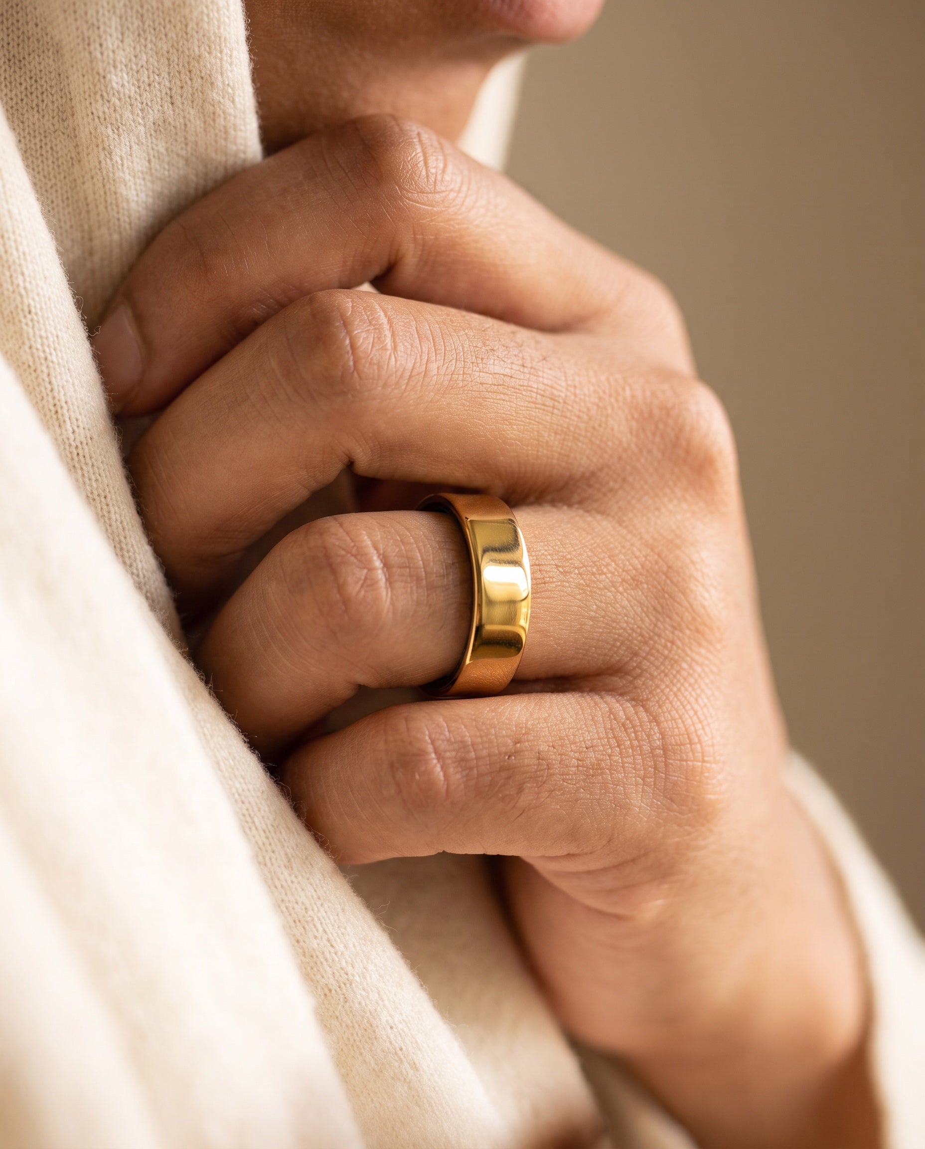 Close-up of a gold Mudrika smart ring worn on a hand, resting against a cream knit sweater